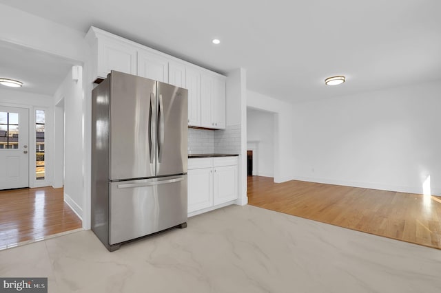 kitchen with light wood finished floors, baseboards, decorative backsplash, freestanding refrigerator, and white cabinetry