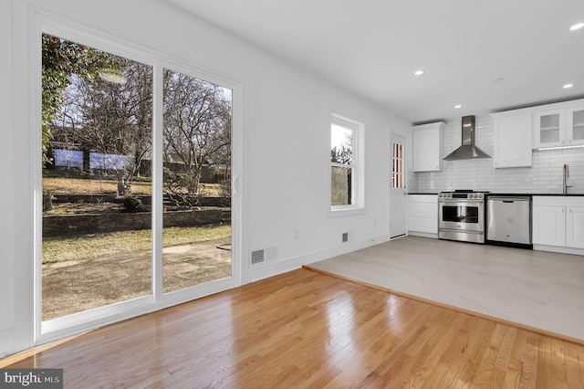 kitchen featuring light wood-style flooring, a sink, appliances with stainless steel finishes, wall chimney exhaust hood, and backsplash