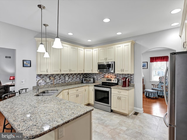 kitchen featuring visible vents, a peninsula, cream cabinets, stainless steel appliances, and a sink