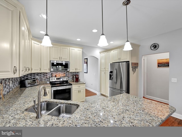 kitchen with arched walkways, stainless steel appliances, a sink, cream cabinetry, and backsplash