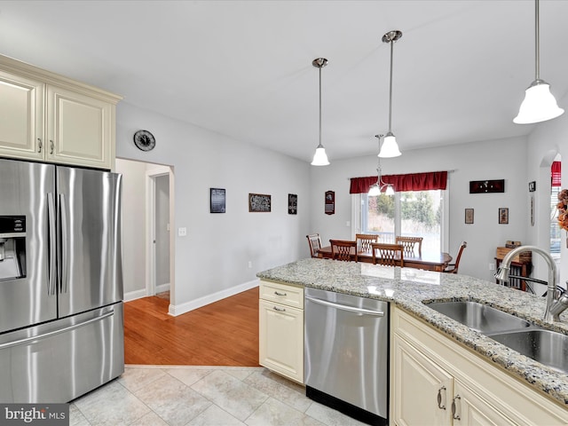 kitchen with arched walkways, cream cabinetry, stainless steel appliances, light tile patterned flooring, and a sink