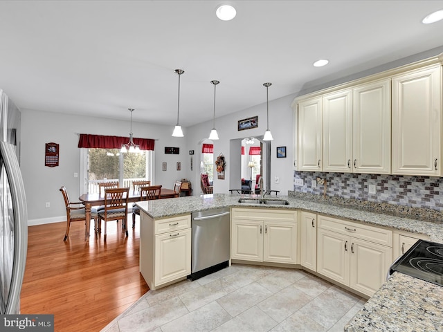 kitchen with appliances with stainless steel finishes, cream cabinetry, a sink, and a peninsula