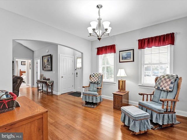 living area with light wood-style floors, baseboards, arched walkways, and a notable chandelier