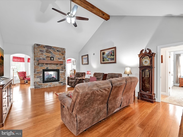 living room with arched walkways, a fireplace, light wood finished floors, high vaulted ceiling, and beamed ceiling