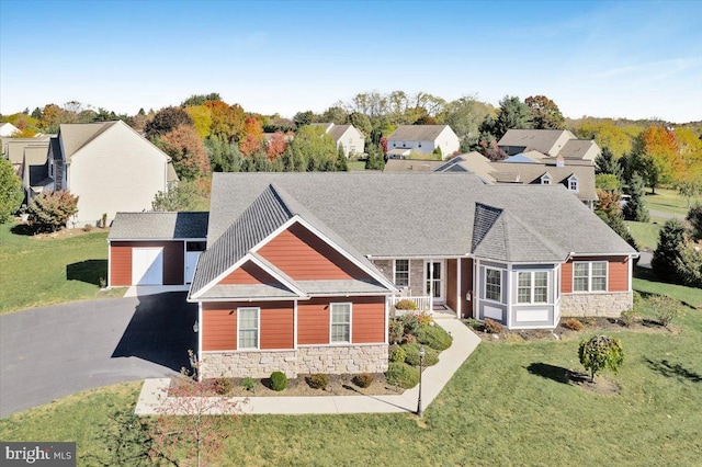 view of front facade featuring roof with shingles, a front yard, a garage, stone siding, and an outdoor structure