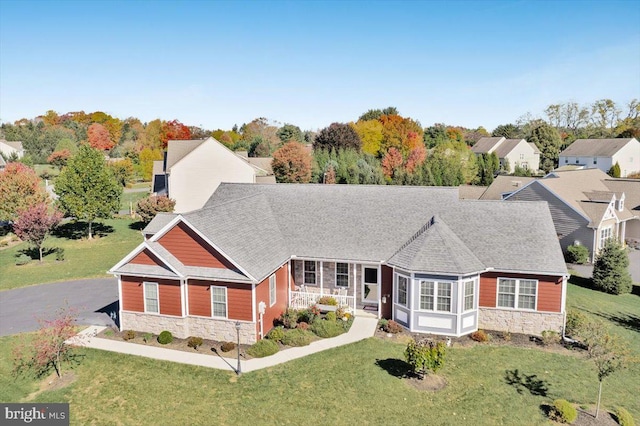 view of front of property featuring stone siding, a front lawn, a shingled roof, and driveway