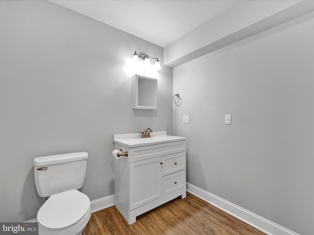 half bathroom featuring vanity, wood finished floors, toilet, and baseboards