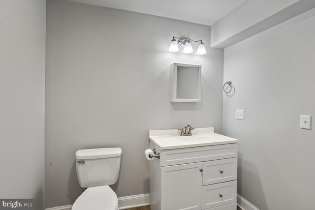 half bath with toilet, baseboards, and vanity