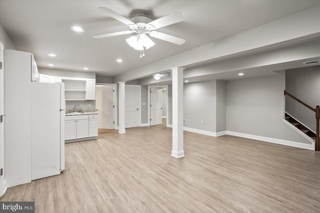 finished below grade area featuring light wood finished floors, a ceiling fan, stairs, a sink, and recessed lighting