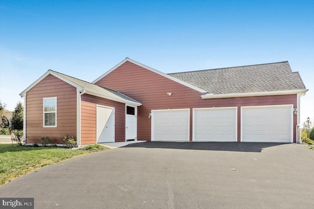 view of front of property featuring aphalt driveway, roof with shingles, an outdoor structure, and a garage