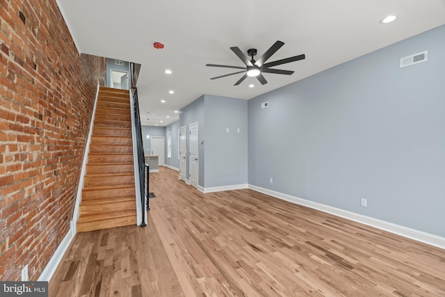 unfurnished living room with light wood finished floors, visible vents, baseboards, brick wall, and stairway