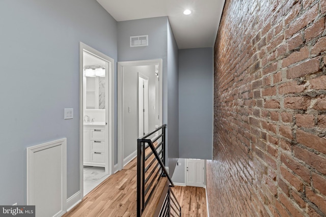 hall with brick wall, an upstairs landing, visible vents, baseboards, and light wood finished floors