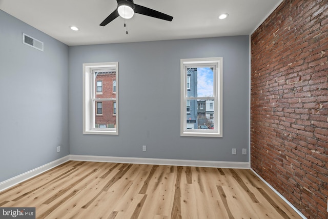 empty room with a healthy amount of sunlight, brick wall, visible vents, and baseboards