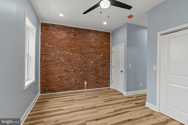 empty room with brick wall, light wood-type flooring, a ceiling fan, and baseboards