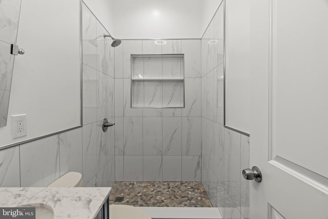 bathroom with toilet, tiled shower, and vanity