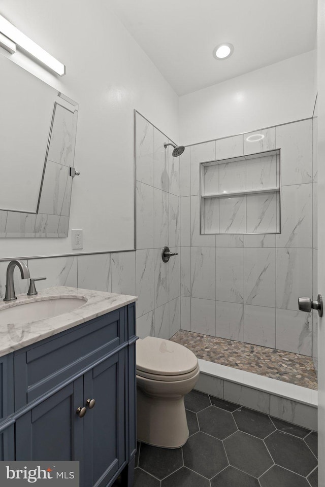 bathroom featuring tiled shower, toilet, tile patterned flooring, vanity, and tile walls