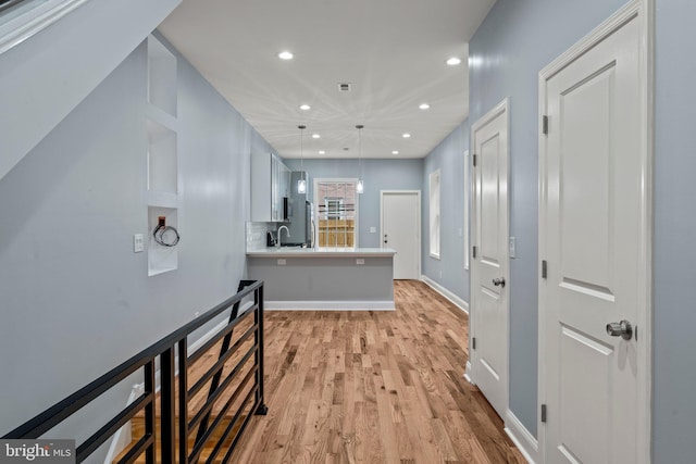 hall with light wood-style floors, recessed lighting, a sink, and baseboards