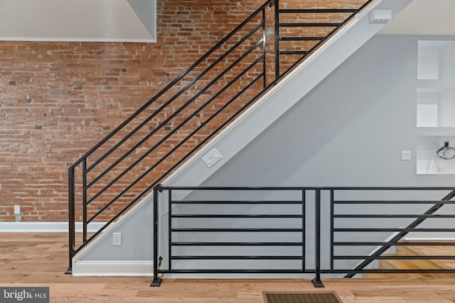 stairway with brick wall, wood finished floors, and baseboards