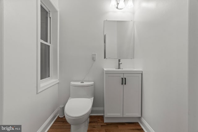 half bath with vanity, wood finished floors, toilet, and baseboards