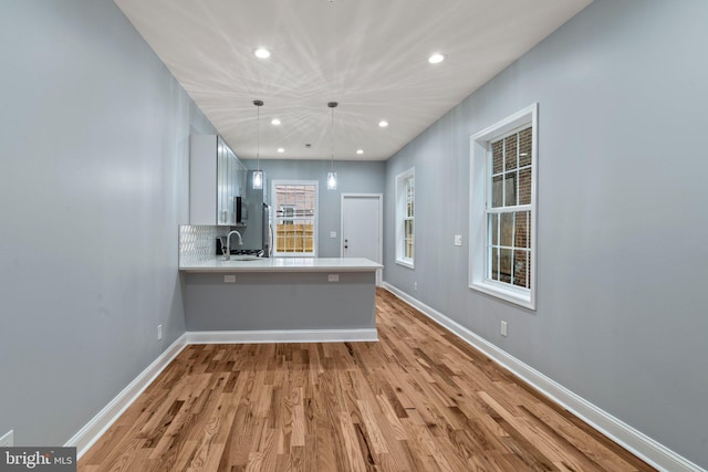 kitchen with a peninsula, light wood-type flooring, baseboards, and light countertops