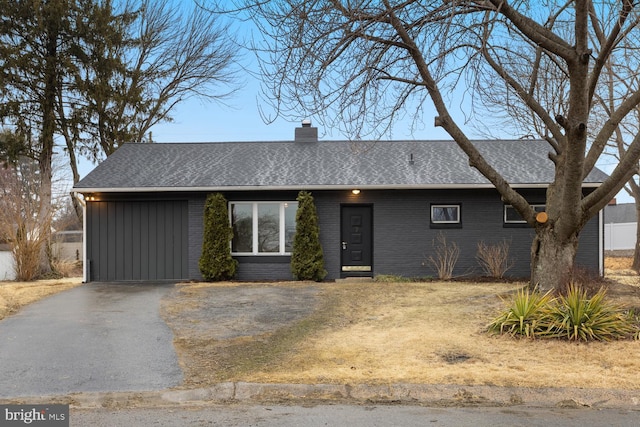 view of front facade featuring driveway, a shingled roof, a chimney, an attached garage, and brick siding