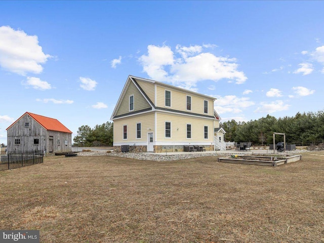 back of property featuring a yard, fence, a barn, a garden, and an outdoor structure