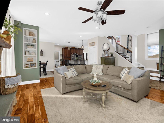 living room featuring baseboards, ceiling fan, stairway, wood finished floors, and recessed lighting