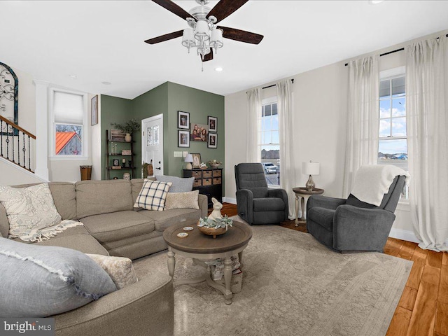 living area with stairs, ceiling fan, baseboards, and wood finished floors