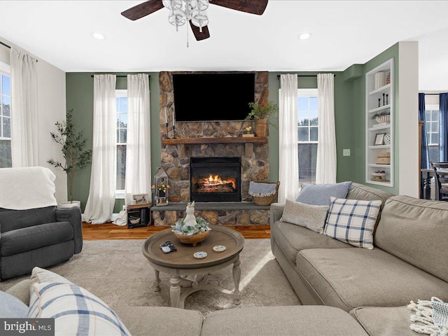 living area with ceiling fan, a stone fireplace, wood finished floors, and recessed lighting