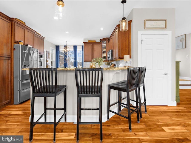 kitchen featuring decorative light fixtures, light wood finished floors, decorative backsplash, appliances with stainless steel finishes, and a peninsula