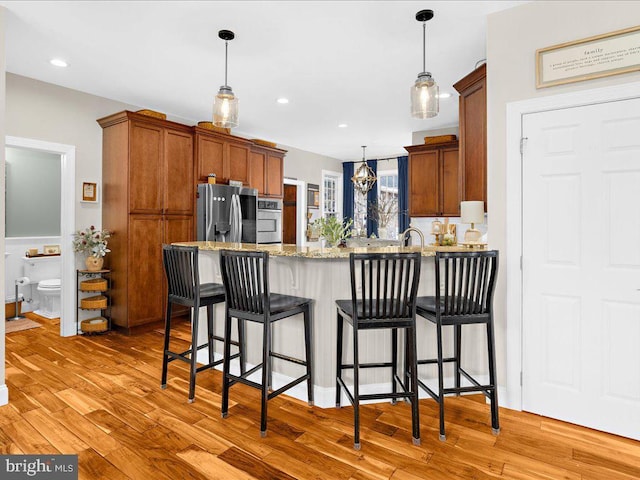 kitchen featuring light wood-style flooring, appliances with stainless steel finishes, brown cabinetry, light stone countertops, and a peninsula