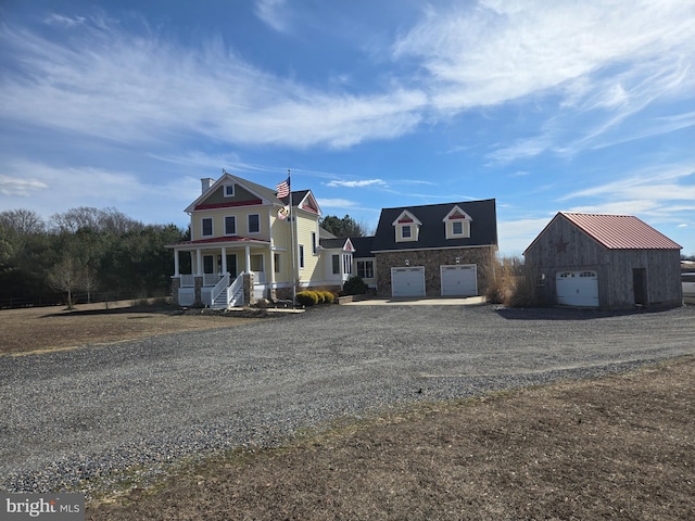 view of front of property featuring a garage, covered porch, stone siding, and gravel driveway