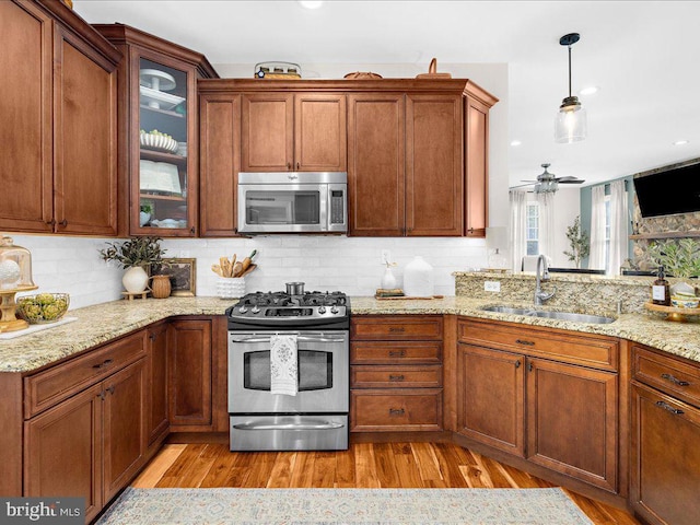 kitchen with a sink, appliances with stainless steel finishes, light wood-type flooring, decorative backsplash, and light stone countertops