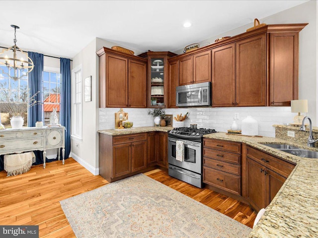 kitchen with stainless steel appliances, a sink, light wood-type flooring, backsplash, and glass insert cabinets