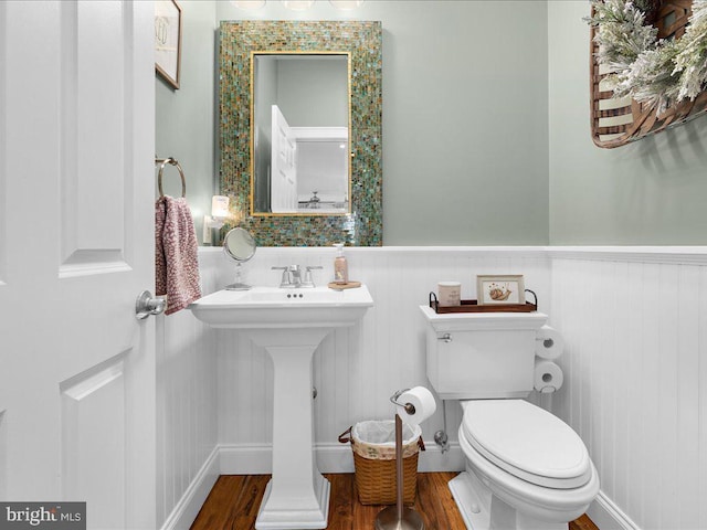 half bath with wainscoting, wood finished floors, and toilet