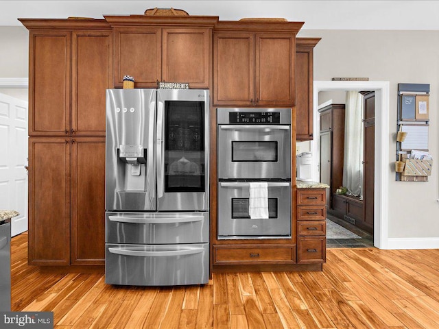 kitchen with baseboards, light wood-style flooring, light stone counters, brown cabinets, and stainless steel appliances