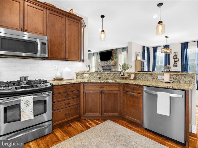 kitchen with wood finished floors, a sink, hanging light fixtures, appliances with stainless steel finishes, and tasteful backsplash