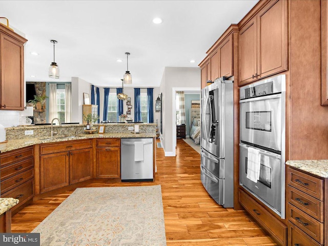 kitchen with light wood-style flooring, appliances with stainless steel finishes, brown cabinets, pendant lighting, and a sink