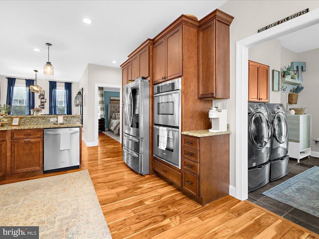 kitchen featuring appliances with stainless steel finishes, washer and clothes dryer, light wood-style floors, and brown cabinets