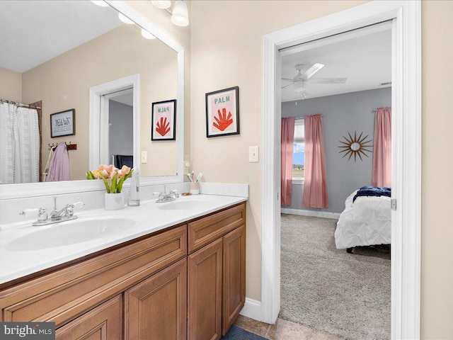 ensuite bathroom featuring double vanity, a sink, a ceiling fan, and baseboards