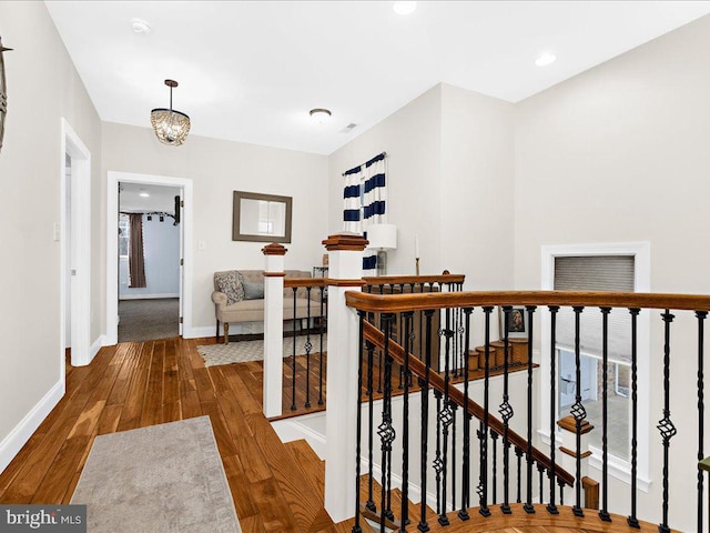 corridor with baseboards, wood finished floors, an upstairs landing, a chandelier, and recessed lighting