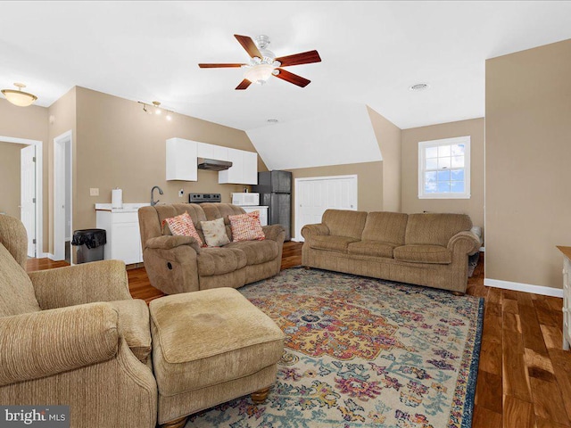 living area featuring dark wood-type flooring, vaulted ceiling, baseboards, and a ceiling fan