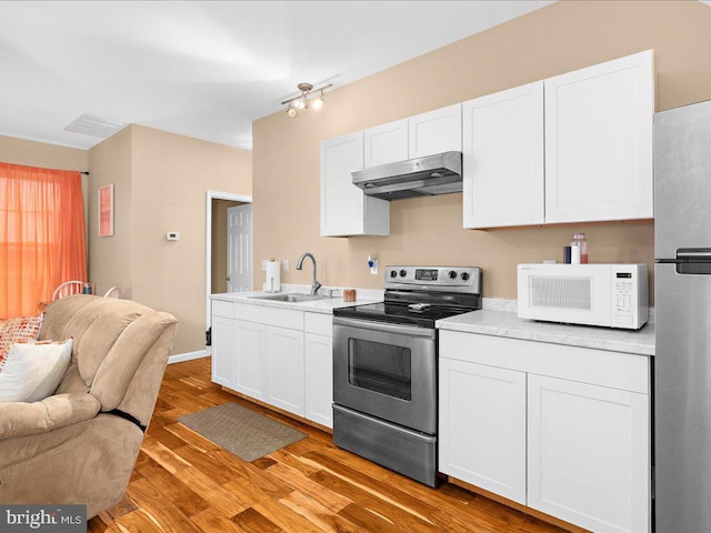 kitchen featuring light countertops, appliances with stainless steel finishes, open floor plan, a sink, and under cabinet range hood