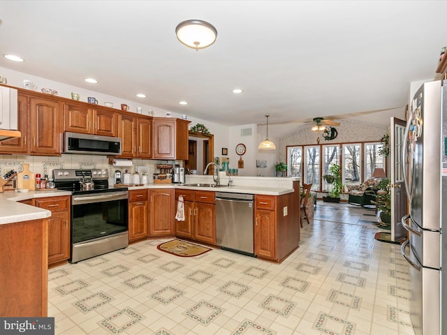 kitchen featuring lofted ceiling, stainless steel appliances, a peninsula, a sink, and brown cabinetry