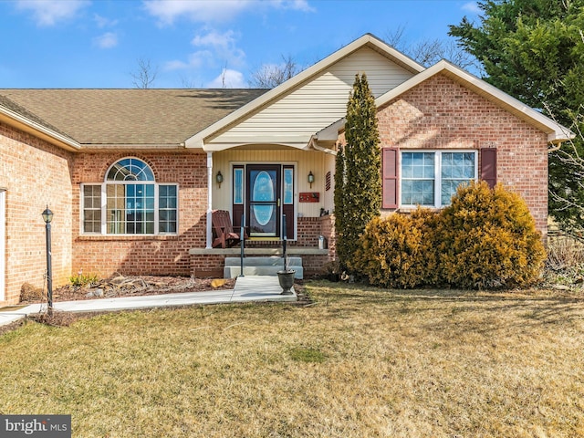 single story home featuring brick siding, a front yard, and a shingled roof