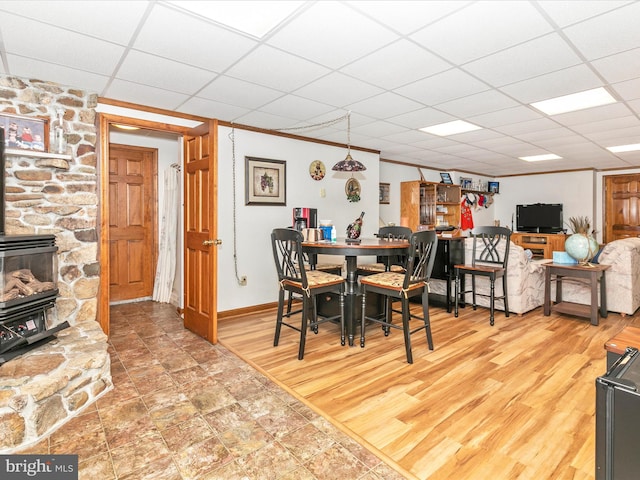 dining space with a drop ceiling, wood finished floors, baseboards, a wood stove, and crown molding