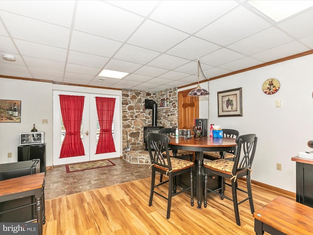 dining area featuring baseboards, a drop ceiling, ornamental molding, wood finished floors, and french doors