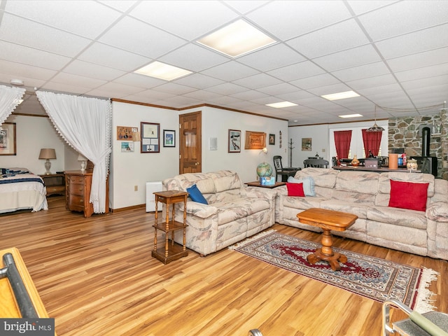 living area with ornamental molding, a paneled ceiling, a wood stove, and wood finished floors