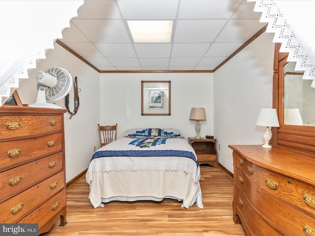 bedroom featuring ornamental molding, light wood-type flooring, a drop ceiling, and baseboards