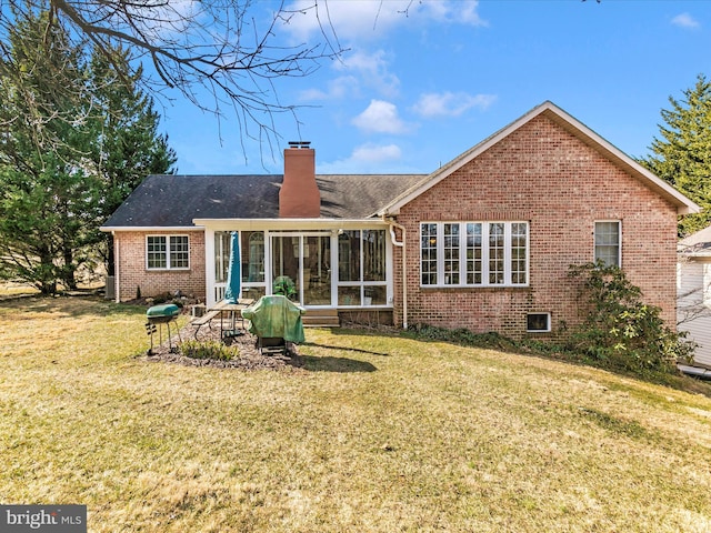 rear view of house with a sunroom, a chimney, a lawn, and brick siding